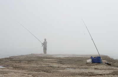 Rear view of man fishing in lake during foggy weather