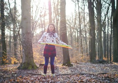 Woman spinning hula hoop while standing on field in forest