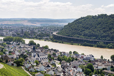 The river rhine flows between the village and the forest covered hills, aerial view.