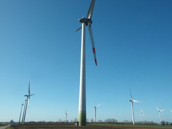 Low angle view of wind turbines on field against sky