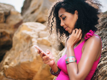 Close-up of young woman using mobile phone while leaning on rock