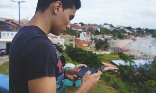 Side view of man using mobile phone against townscape