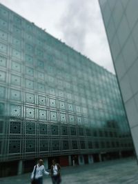 Low angle view of people on glass building against sky