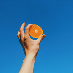 Close-up of hand holding apple against blue sky