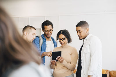 Female computer hacker showing digital tablet to male coworkers while standing against wall in office