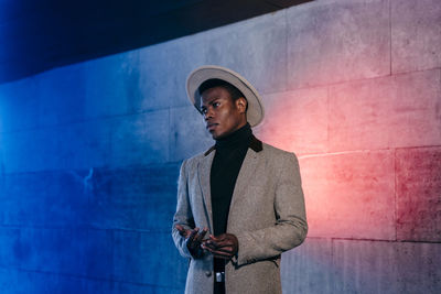 Young man looking away while standing against wall