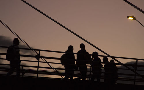 Silhouette people standing on bridge against sky during sunset