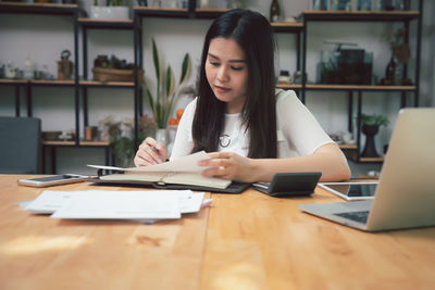 Young woman using phone while sitting on table