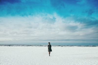 Woman standing at baltic seashore against cloudy sky during winter