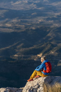 Young woman standing on rocks on top of a mountain looking over.