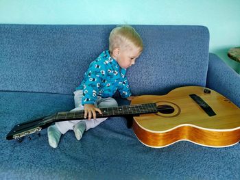 Little boy on a blue couch looks at a retro guitar with interest