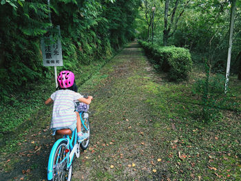 Girl riding bicycle on road amidst trees