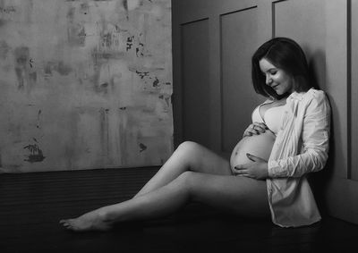 Pregnant woman touching her belly while sitting on hardwood floor at home