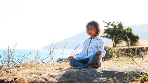 Full length of girl sitting on land against sky