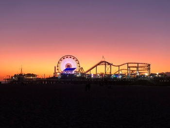 Illuminated ferris wheel against sky at sunset