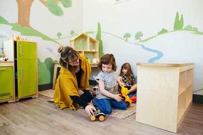 Teacher sitting on ground pushes a toy car showing a student