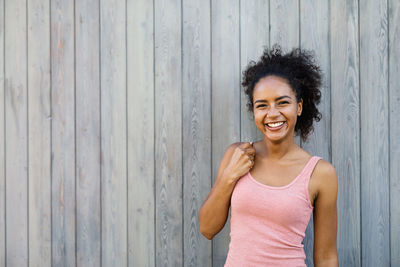 Portrait of cheerful young woman standing against gray wooden wall