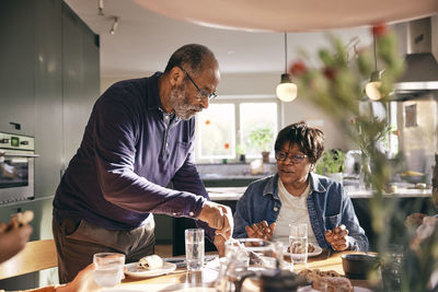 Senior man serving food to woman sitting at dining table in home