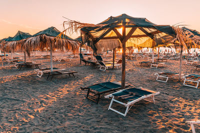 Chairs on beach by sea against sky during sunset