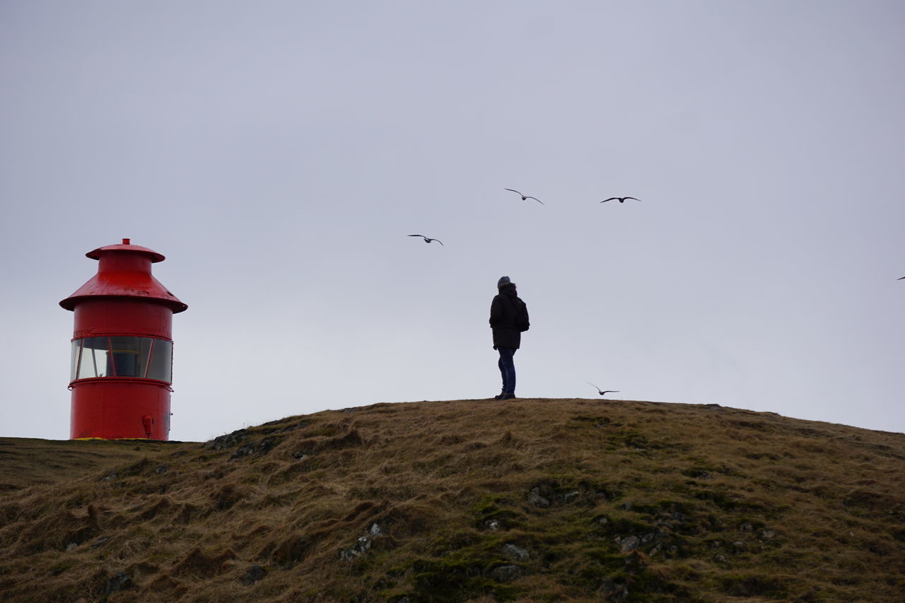 REAR VIEW OF MAN STANDING BY LIGHTHOUSE