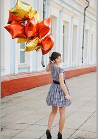 Full length of woman holding helium balloons while standing on footpath