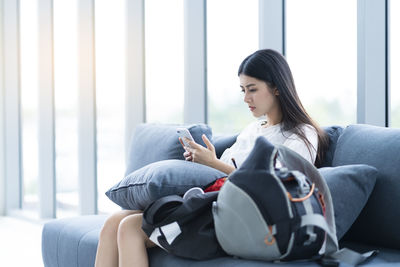 Young woman using mobile phone while siting on sofa at home