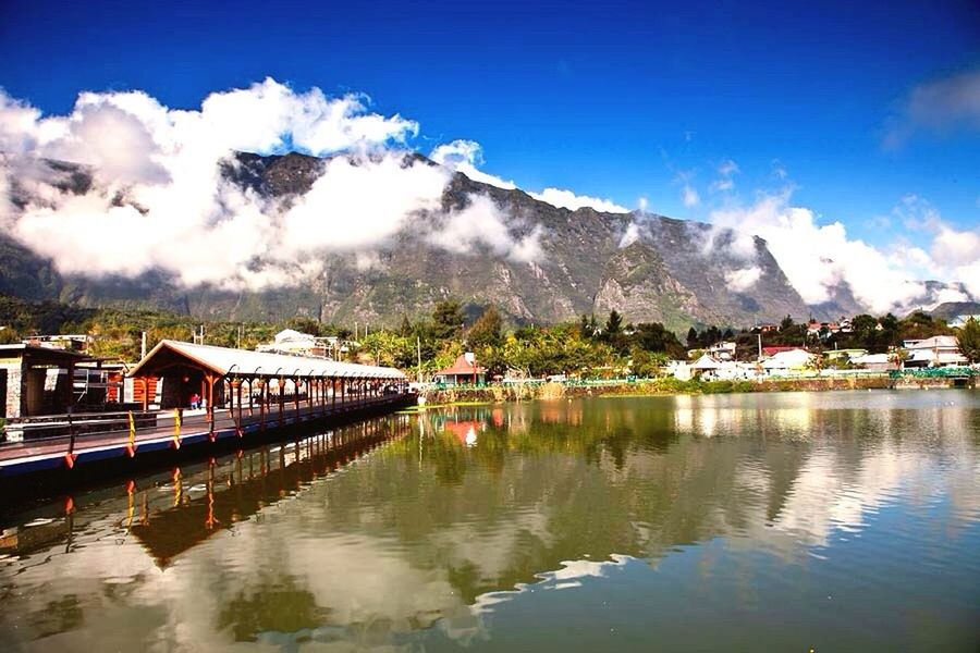 mountain, water, architecture, built structure, mountain range, building exterior, sky, waterfront, cloud - sky, lake, house, cloud, reflection, river, scenics, nature, town, cloudy, beauty in nature, residential structure