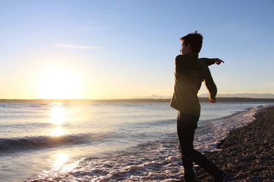 Young man on beach against clear sky during sunset