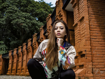 Portrait of young woman standing against building