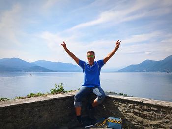 Portrait of mature man sitting on retaining wall against lake