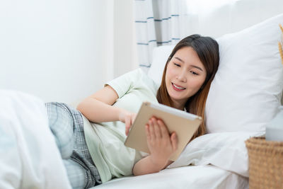 Young woman using mobile phone while lying on bed at home