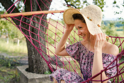 Smiling young woman wearing hat sitting on hammock