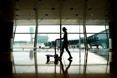 Silhouette person standing at airport seen through glass window