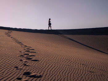 Man standing on sand dune in desert against sky