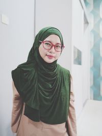 Portrait of smiling woman wearing hijab standing against wall