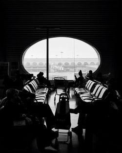 People sitting in departure area against window at chongqing jiangbei international airport