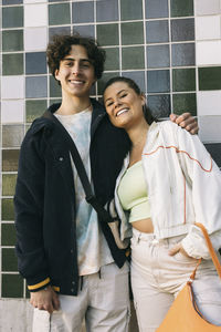 Smiling teenage boy standing with female friend against tiled wall