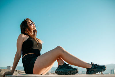 Side view of girl sitting against sky