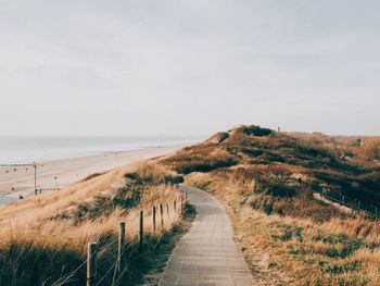 Footpath leading towards sea against sky