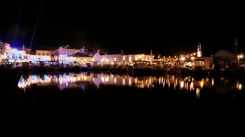 Illuminated buildings by sea against sky at night