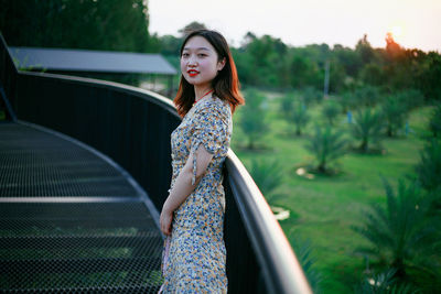 Portrait of young woman standing by railing