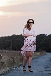 Full length portrait of woman standing by road against sky