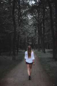 Rear view of woman walking on road in forest