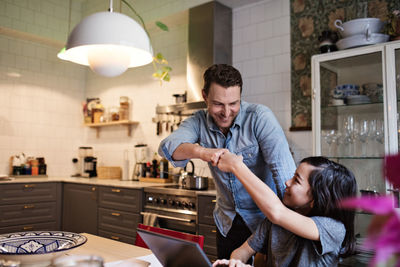 Smiling son bumping fist with father while studying at home