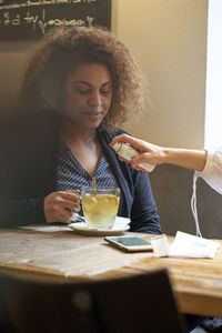 Woman looking at friend spraying over drink at table