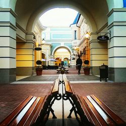 Rear view of man walking on footpath by benches amidst buildings