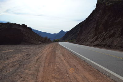 Empty road amidst mountains against sky