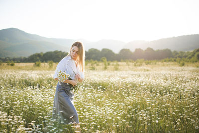 Attractive blonde female girl pick up camomile flower walk in field over green nature outdoor