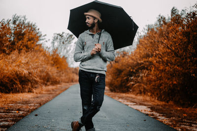 Full length of man standing with umbrella on road during autumn