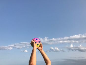 Close-up of hands holding a ball against blue sky